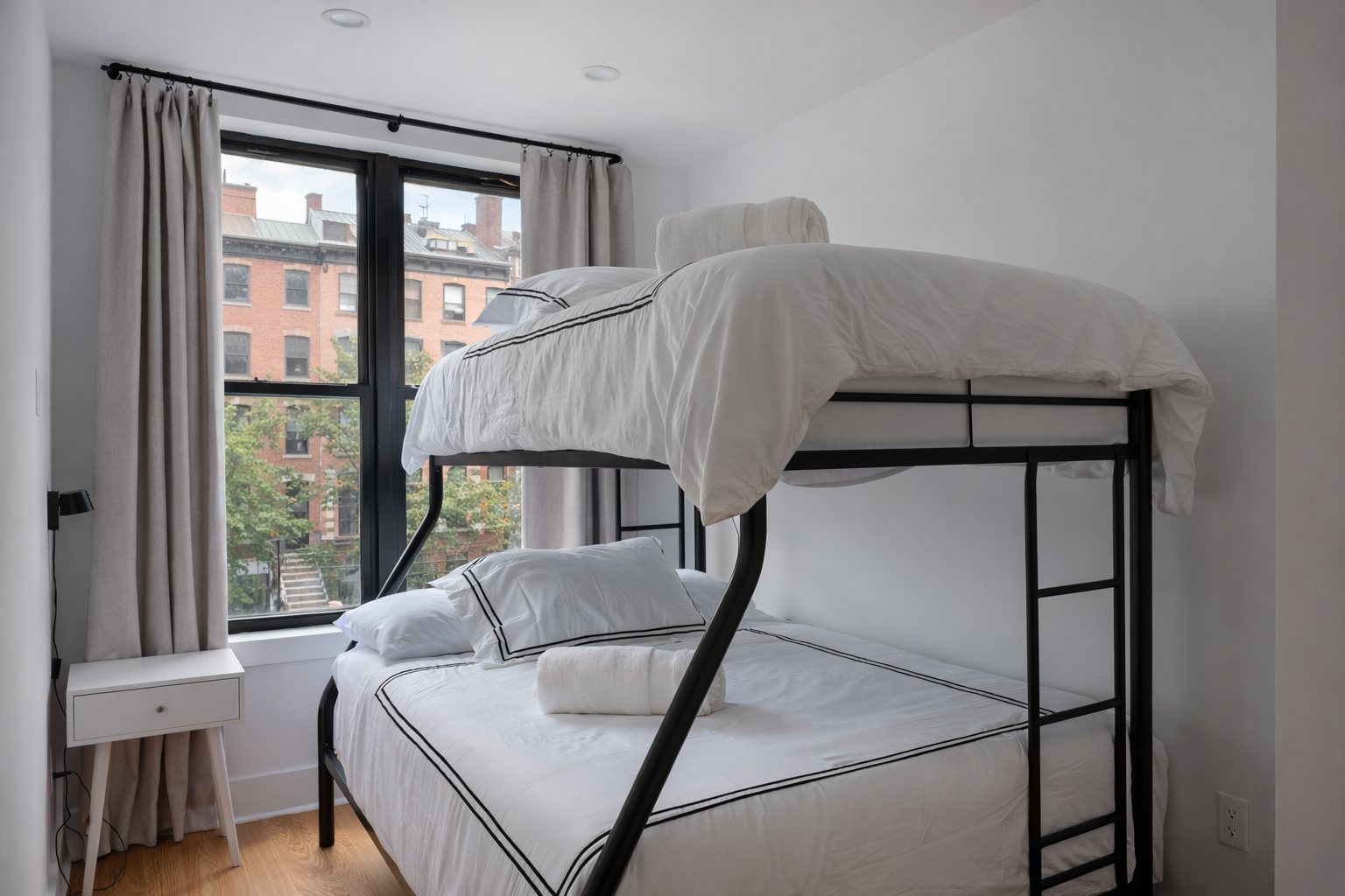 Bunk room with a twin-over-full bunk bed and a window onto brick row houses