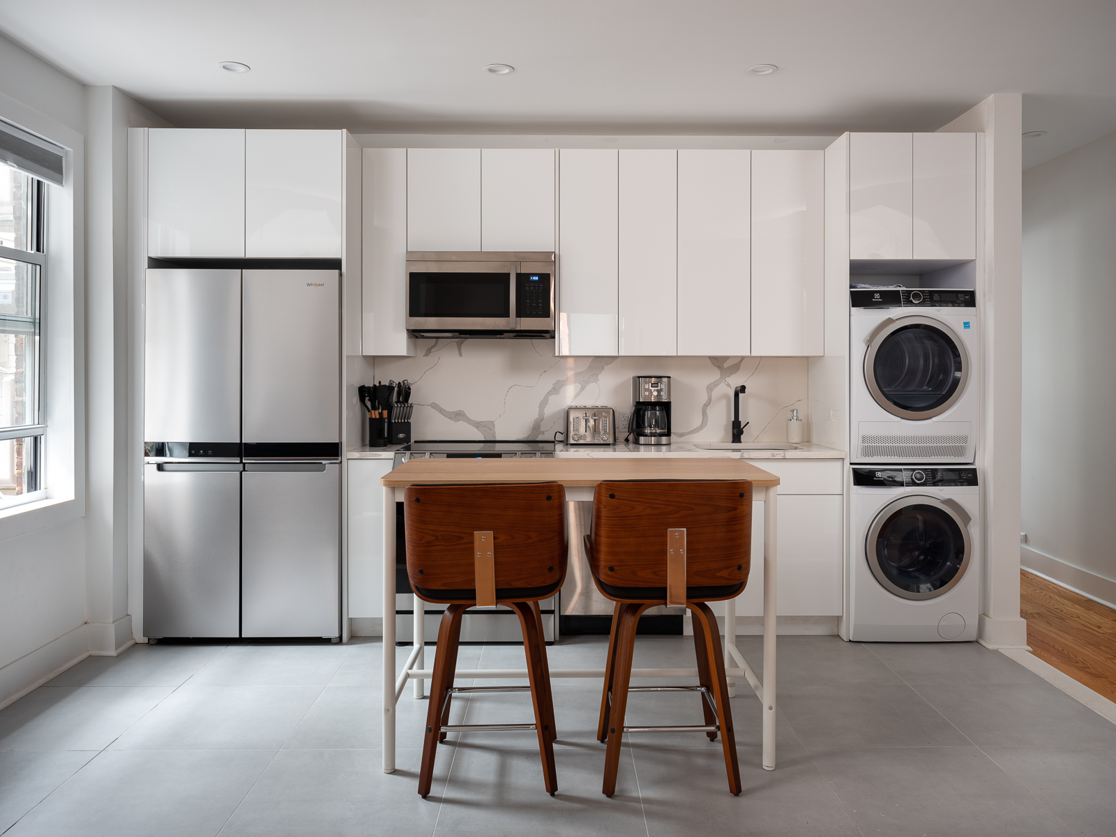 White gloss kitchen with marble backsplash, stainless appliances and stacked washer and dryer