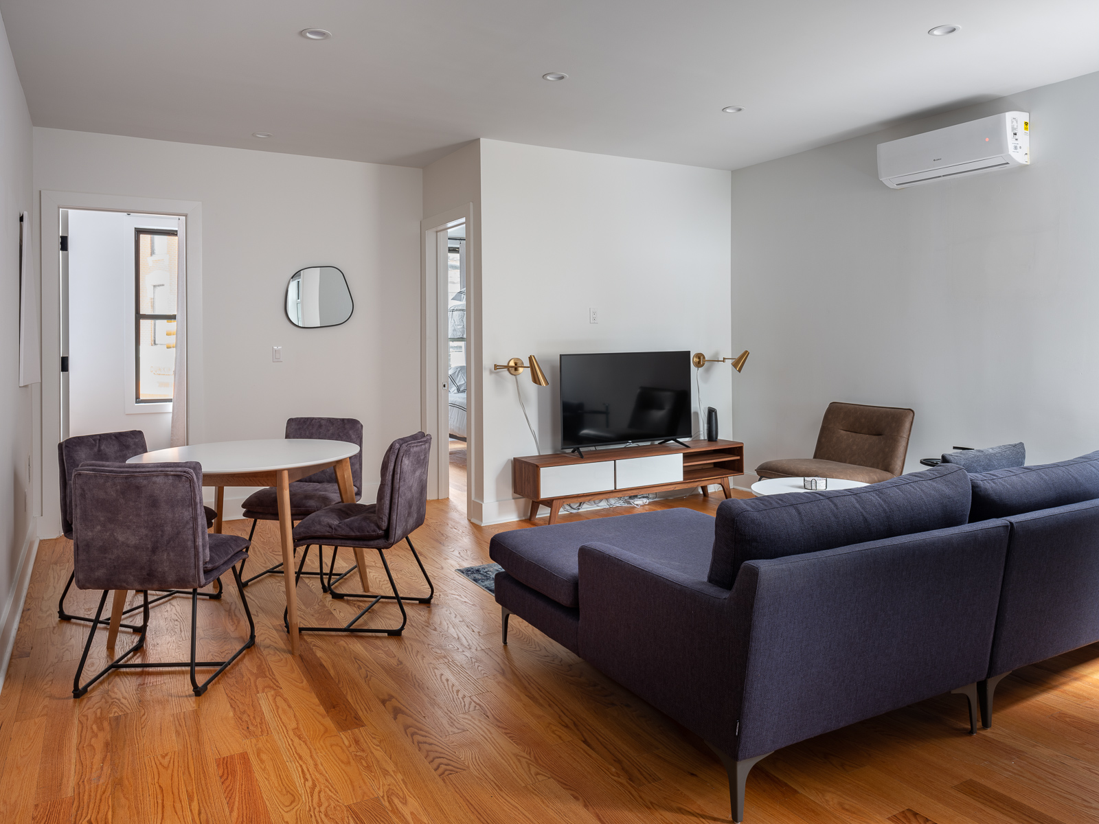 Sunlit living and dining room at Greenpoint House with oak floors, a navy sectional and a round dining table