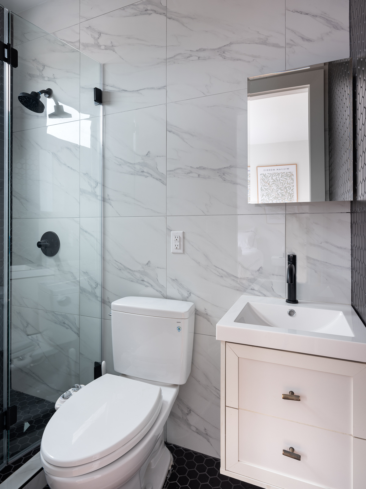 Marble-tiled bathroom with glass shower, matte black fixtures and floating vanity