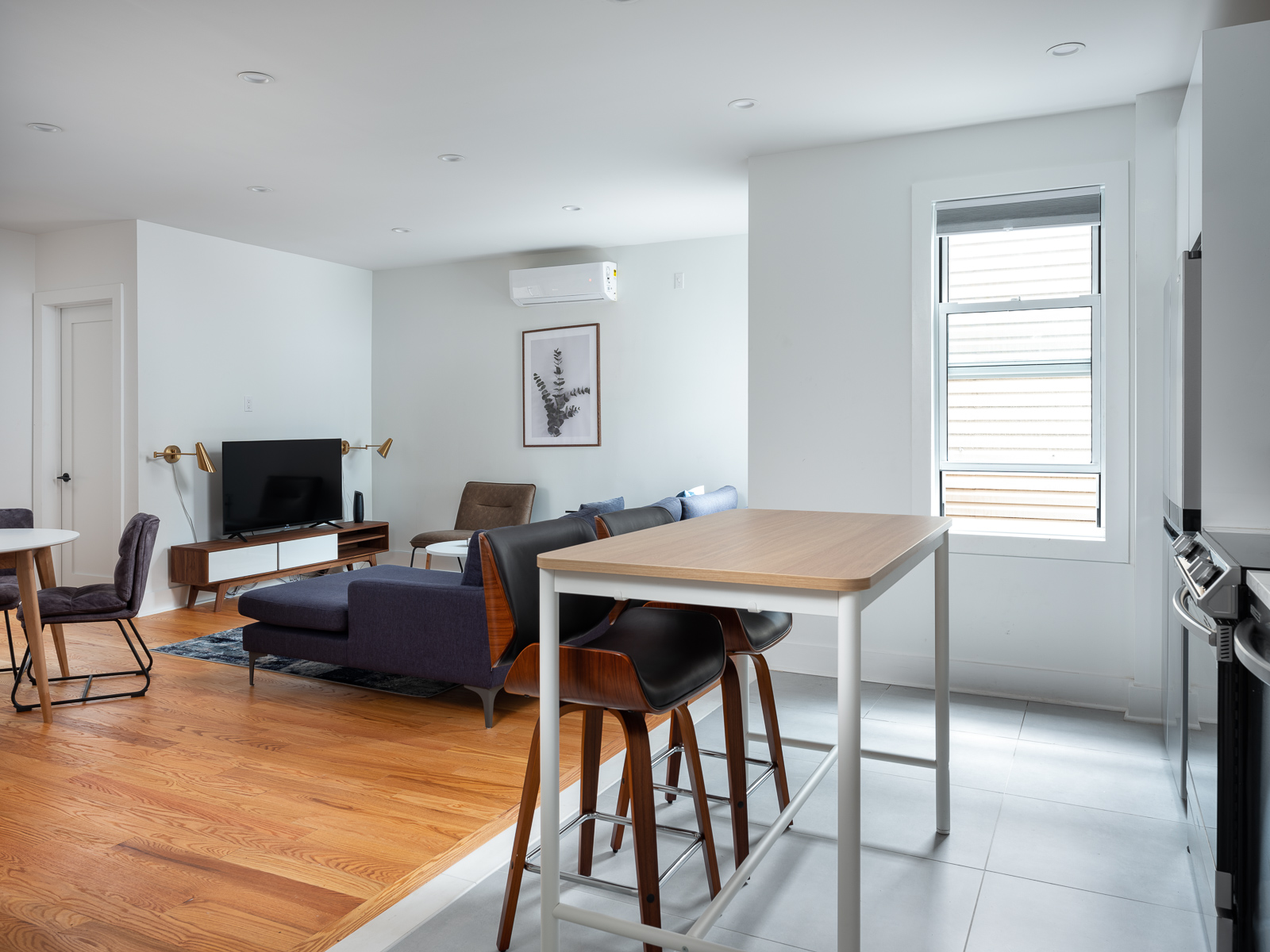 Open-plan living room and kitchen with oak floors, navy sectional and walnut counter stools
