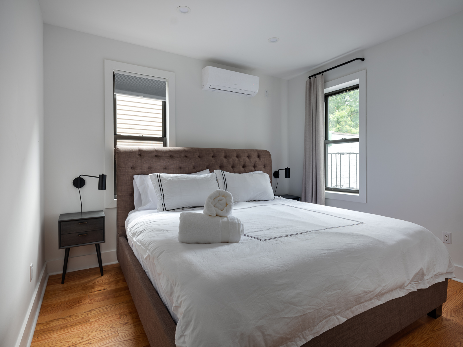 King bedroom with tufted headboard, crisp white linens and black wall sconces
